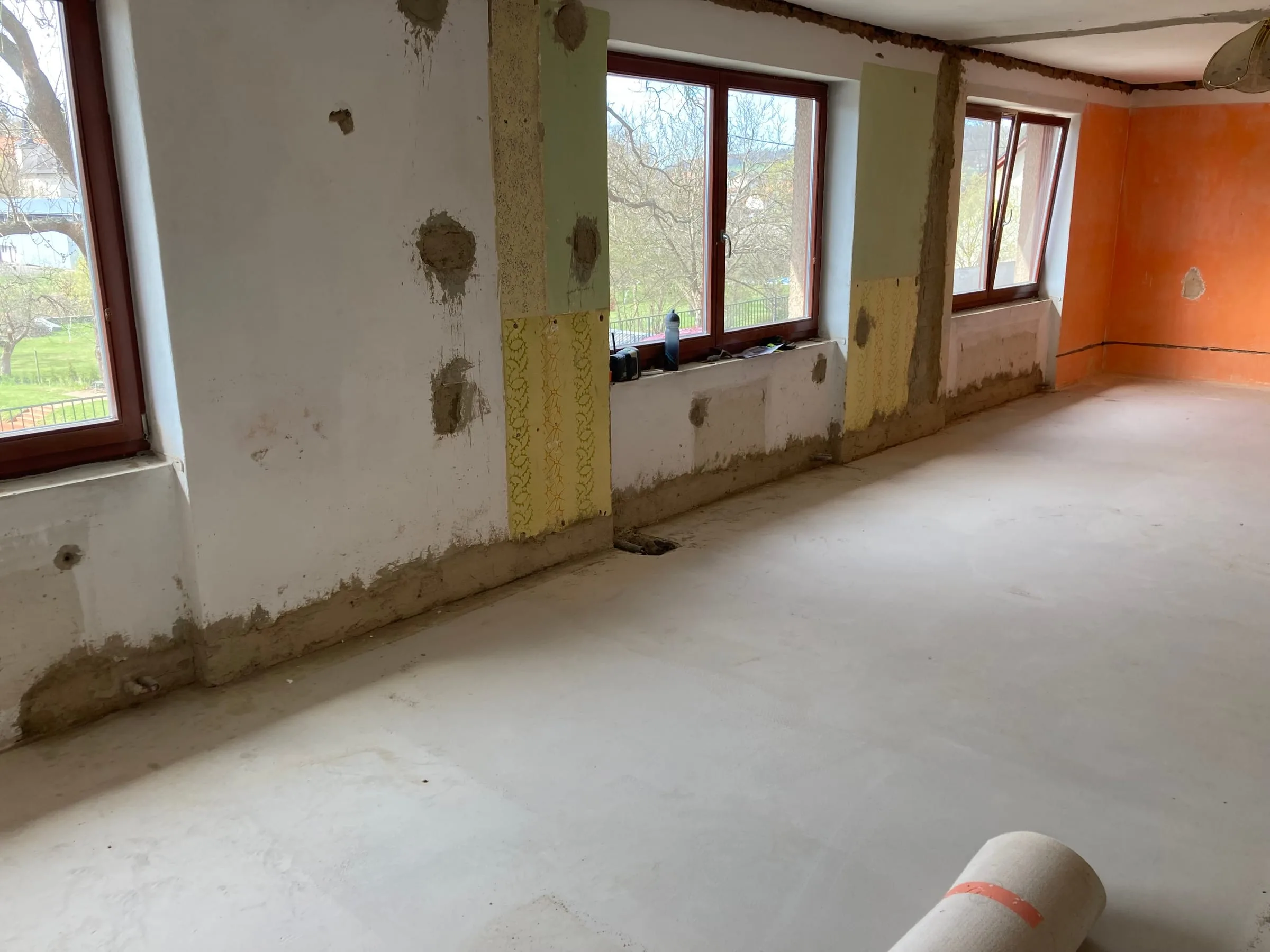 Stěna s&nbsp;okny se zapravenými drážkami po nových rozvodech elektřiny a&nbsp;vyrovnaná podlaha