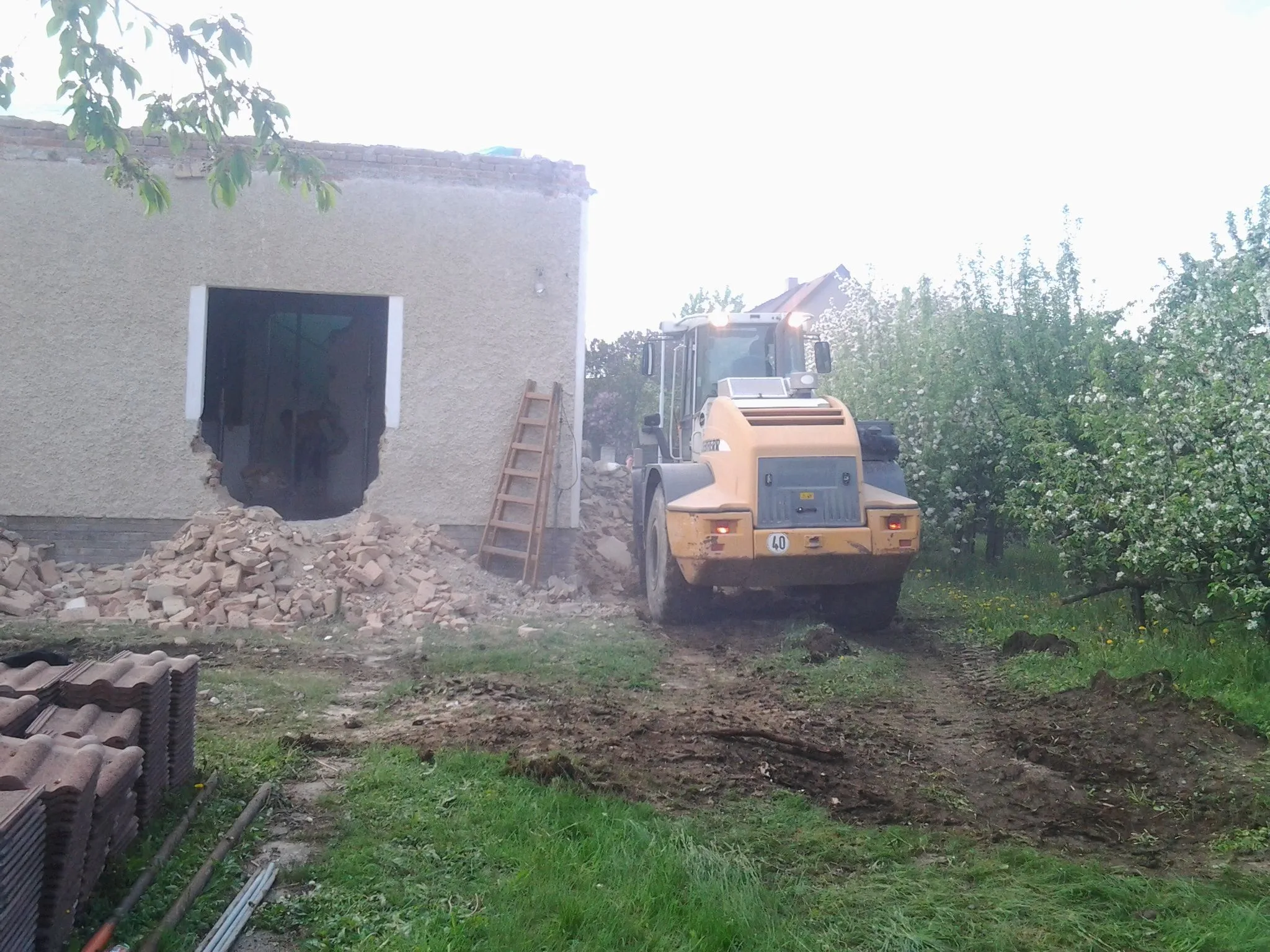 Nakladač u&nbsp;bouraného přístavku, vybouraná zeď a&nbsp;hromada cihel