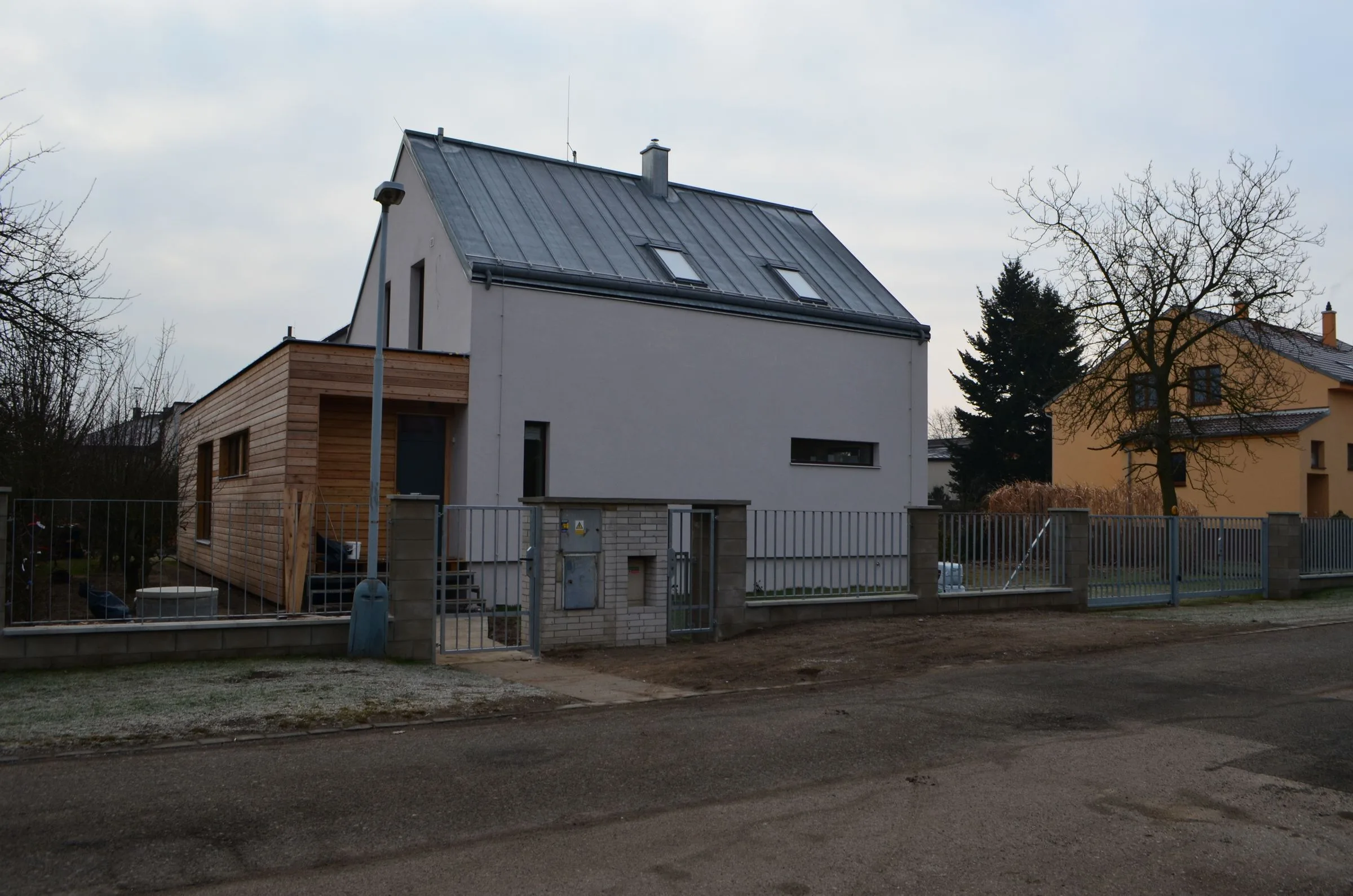 Hotový dům od ulice s&nbsp;novým plotem a&nbsp;dřevěnou přístavbou