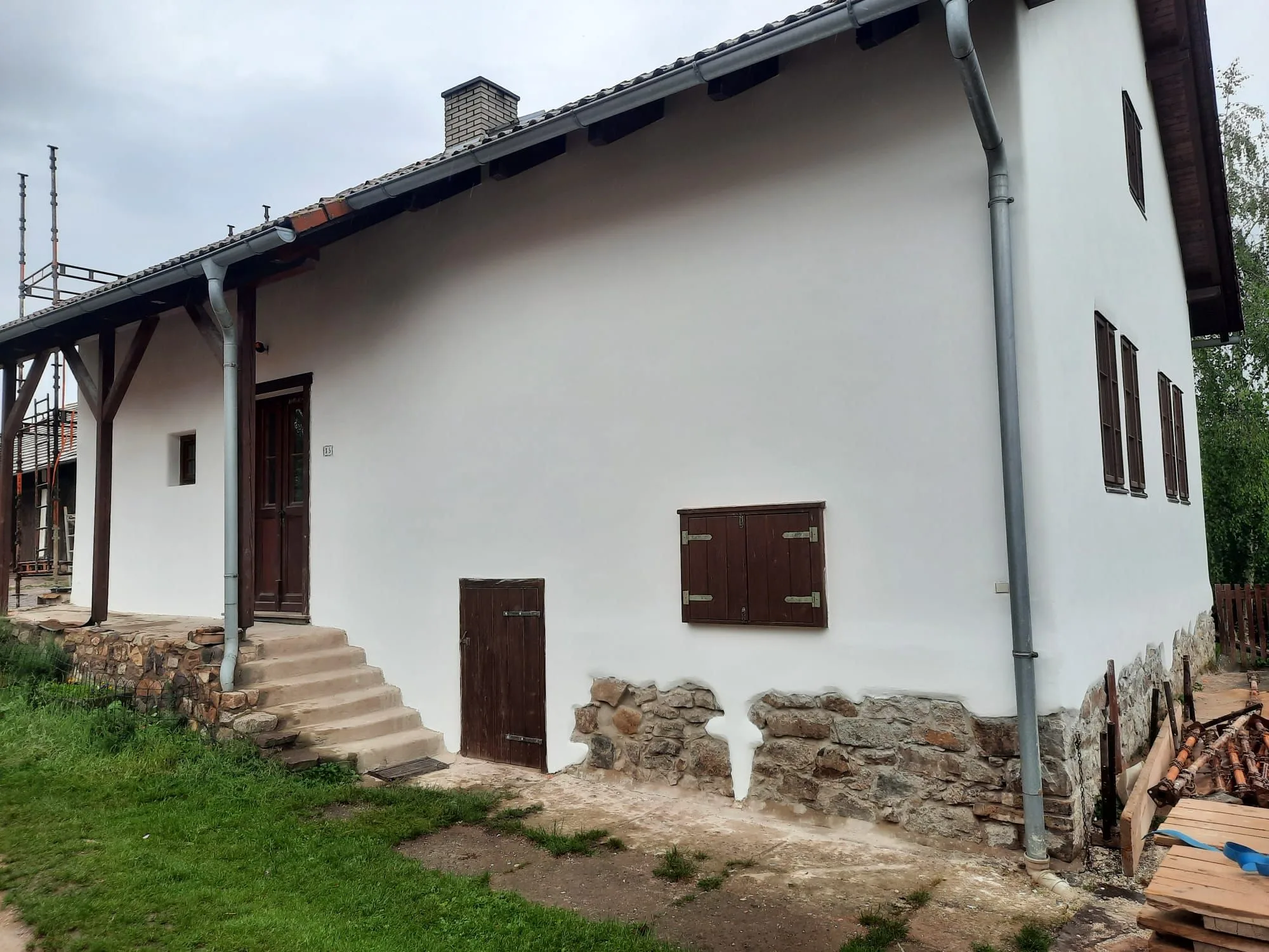 Bílá fasáda staršího domu s&nbsp;okenicemi a&nbsp;kamenným soklem