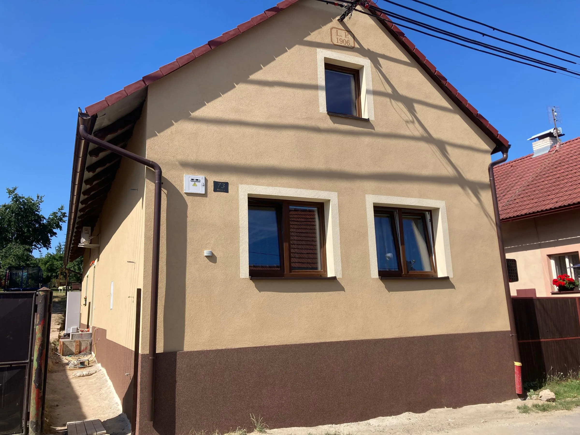 Štít domu s&nbsp;béžovou fasádou a&nbsp;hnědým soklem
