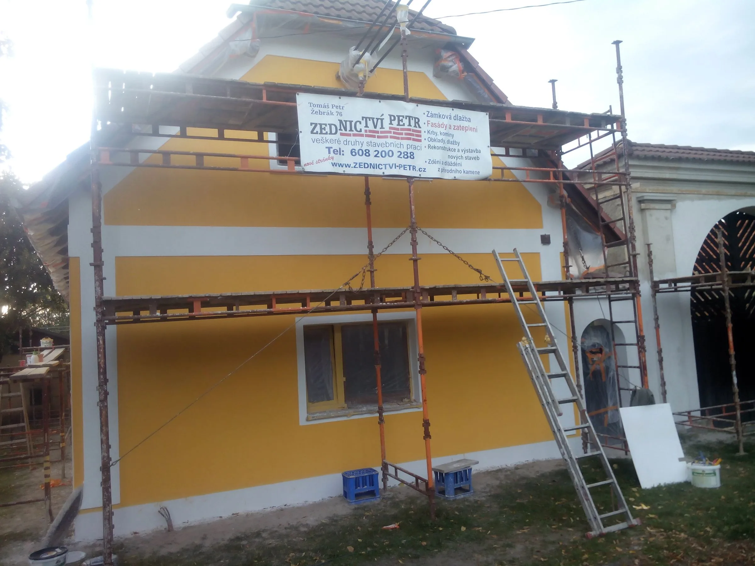 Lešení u&nbsp;štítu domu s&nbsp;cedulí Zednictví Petr a&nbsp;novou žlutou omítkou