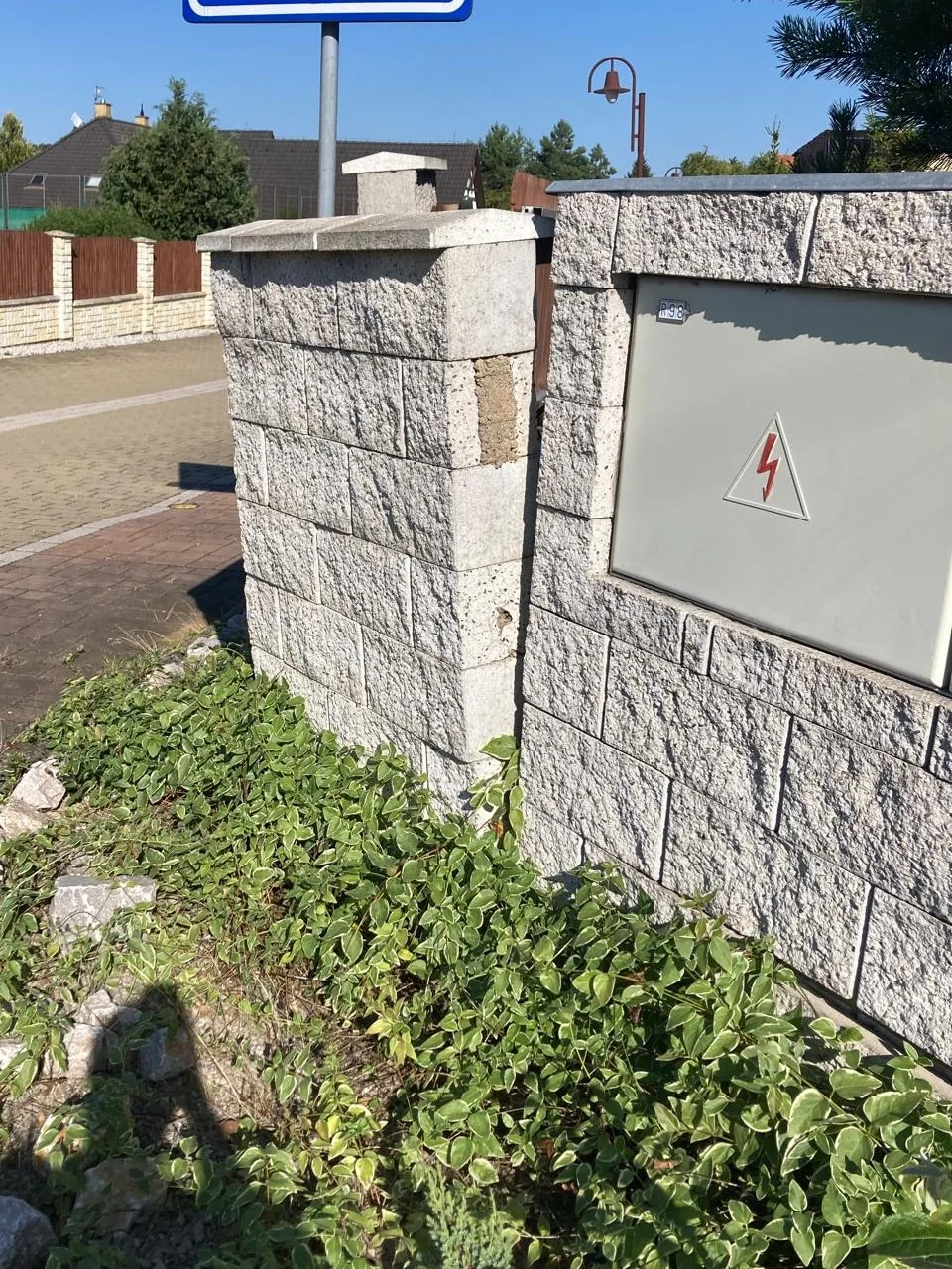 Sloupek cizího plotu odkloněný od rovné zdi, v&nbsp;rohu chybí kus tvárnice