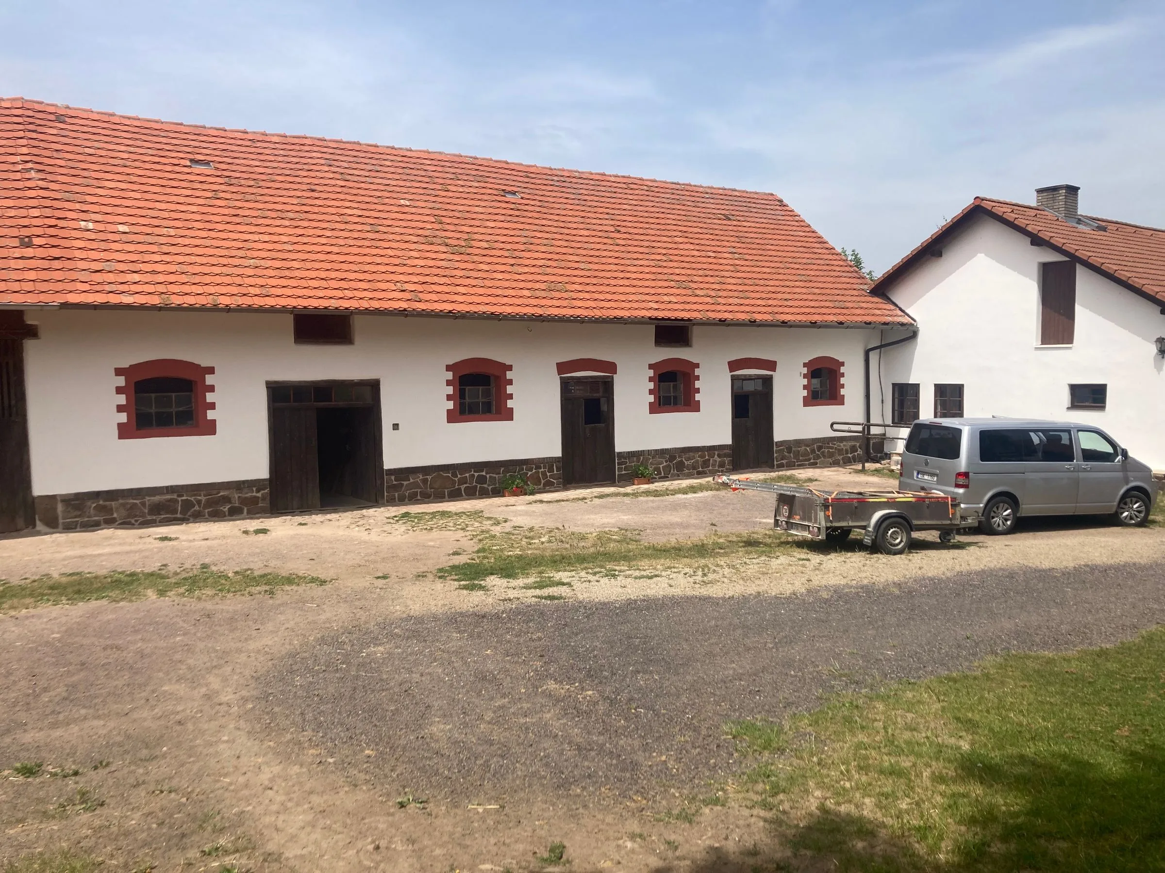 Stodola a&nbsp;obytný dům statku po opravě fasády, okna s&nbsp;červenými šambránami